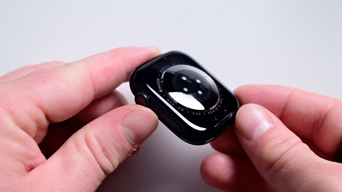 Hands holding the back of a black smartwatch, displaying its sensors and glossy finish.