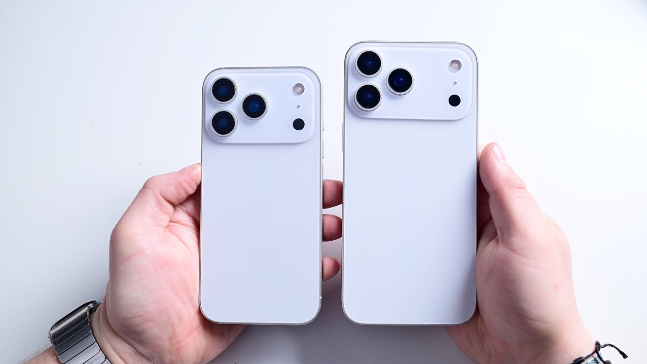 Two hands holding two white smartphones with triple cameras positioned against a plain background.