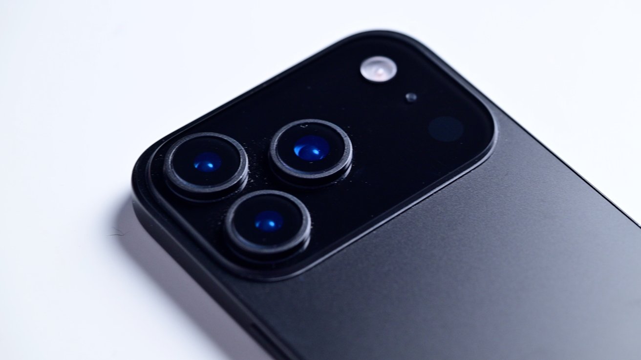 Close-up of a smartphone's back with three camera lenses and a flash on a sleek, black surface.