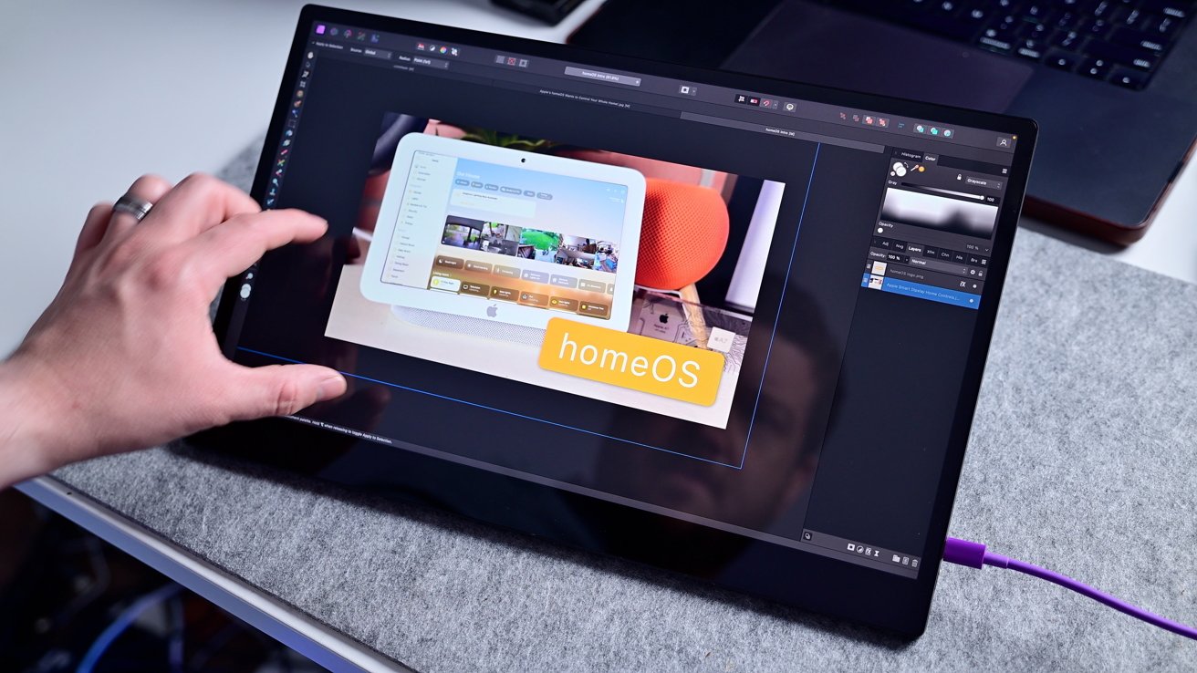 A person interacts with a tablet displaying a user interface labeled 'homeOS,' featuring a control panel and home screen, with a computer visible in the background.