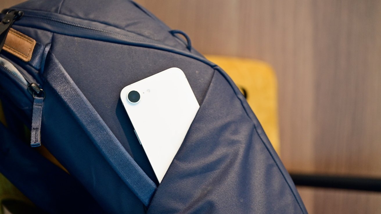 A white smartphone partially protrudes from a pocket on a blue backpack.