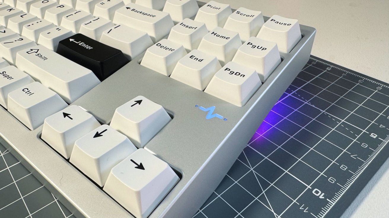White keyboard with a black Enter key on a cutting mat, blue light under the edge, and visible arrow keys.