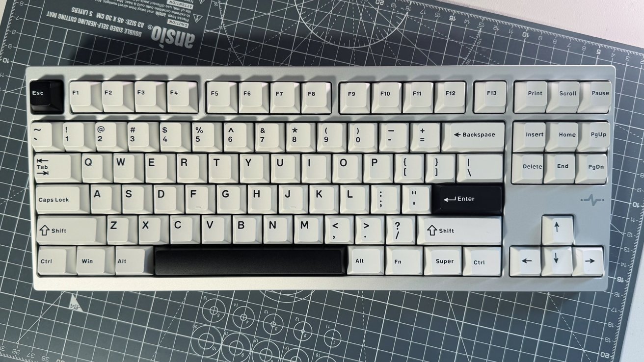 White mechanical keyboard with black Enter and Escape keys, function keys, arrow keys, and number row; gray background with grid and circular patterns.