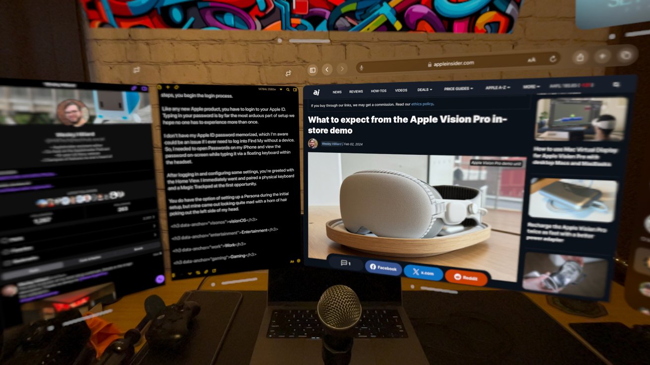 Desk with computer monitors, one displaying an article about Apple Vision Pro, surrounded by gaming controllers, a microphone, and colorful wall art in the background.