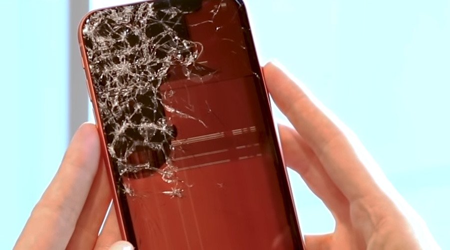 Close-up of hands holding a smartphone with a heavily cracked screen displaying red and black colors.