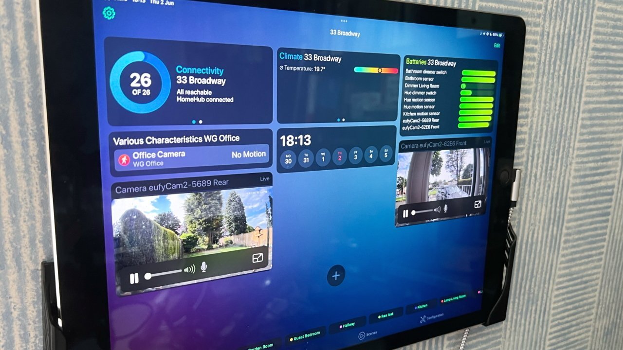 Wall-mounted tablet displaying home automation dashboard with connectivity, climate, and battery status. Live camera feeds show outdoor views. Time and date are visible at center.
