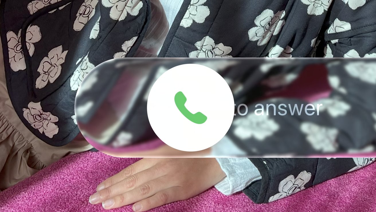Hand rests on pink surface; phone icon and partial text overlay, floral pattern in the background.