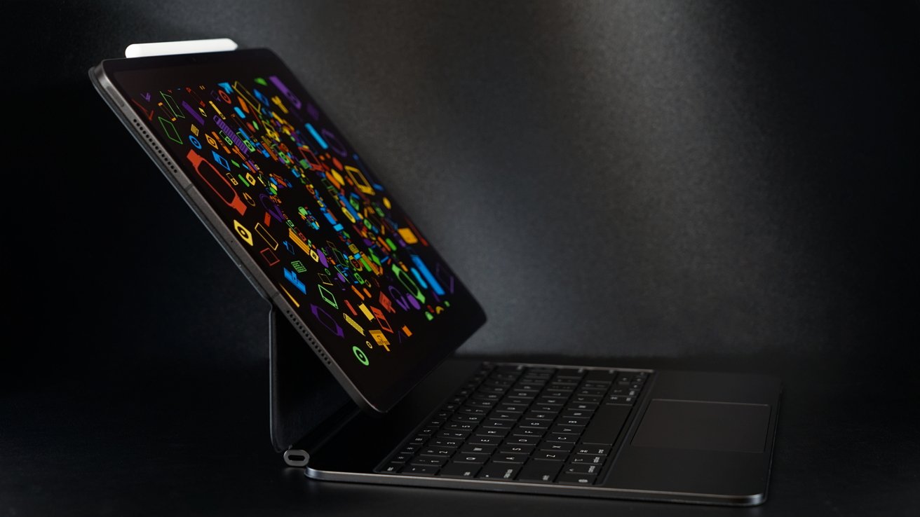 Open laptop with a colorful geometric pattern on the screen against a dark background, featuring a visible keyboard and trackpad.
